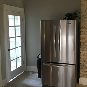 A stainless steel Whirlpool refrigerator in a kitchen with a white door and a brick wall. - 2-bedroom apartment in enchanting Milwaukee with AC comfort (Milwaukee)