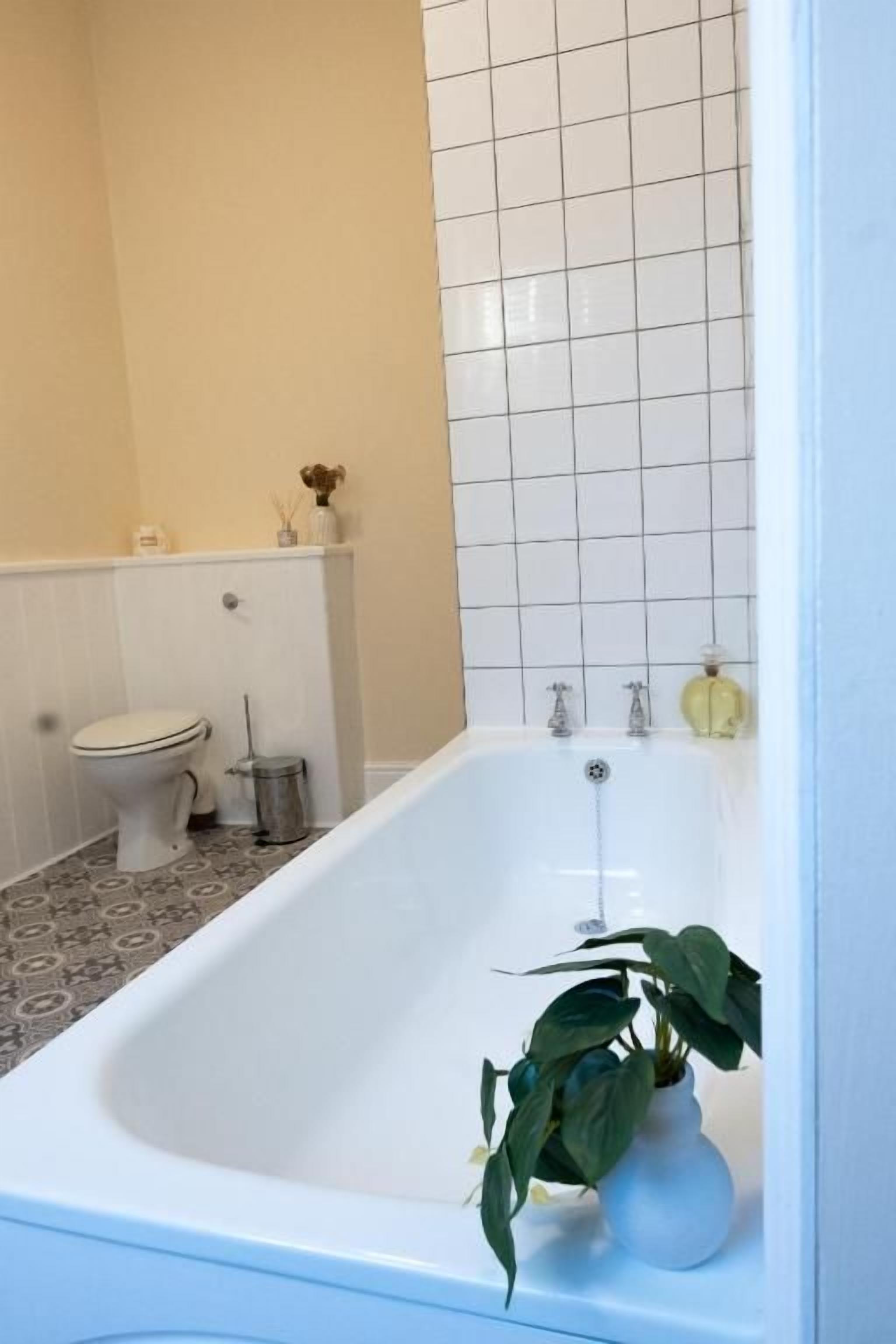 A bathroom with a white bathtub, a toilet, and a tiled wall.