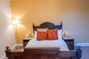 A bed with a wooden headboard, two bedside tables with lamps, and a plain wall. - UpBuxton (Buxton)
