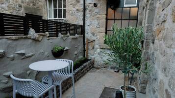 Un patio de piedra con una mesa redonda y dos sillas, una planta en maceta y un pequeño árbol.