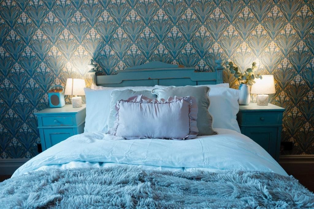 A bed with a fluffy white blanket, two bedside lamps, and a patterned wallpaper.