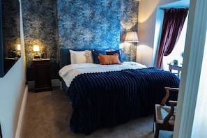 A bedroom with a large bed, a nightstand, a lamp, and a chair.