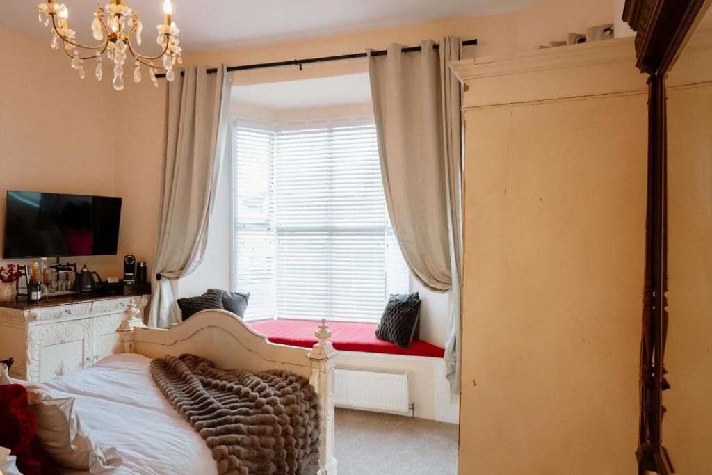A bedroom with a bed, a television, a window with curtains, and a radiator.