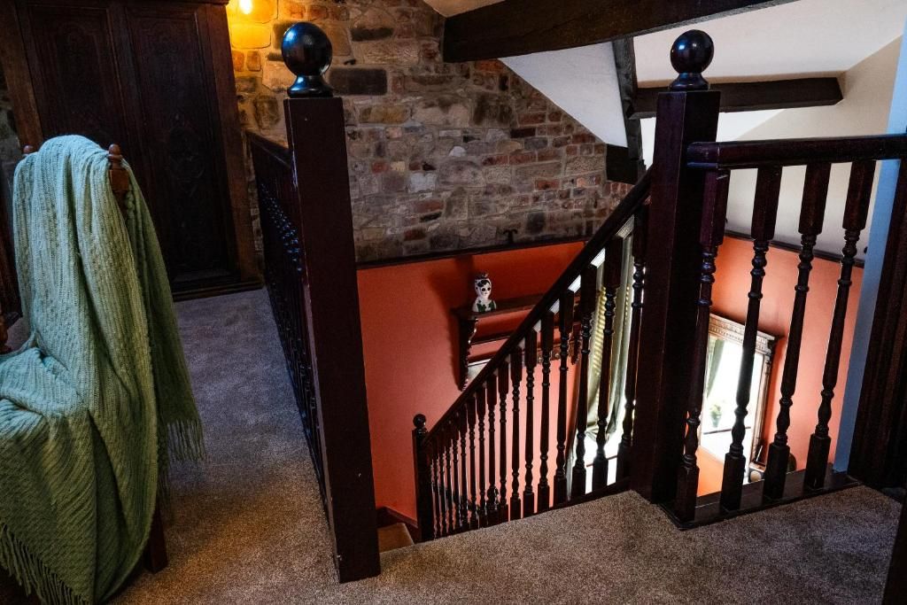 Un escalier doté d’une rampe et de balustrades en bois, menant à un niveau supérieur avec un mur en pierre et un mur rouge.