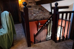 A staircase with a wooden handrail and balusters, leading to an upper level with a stone wall and a red wall. - UpBuxton (Buxton)