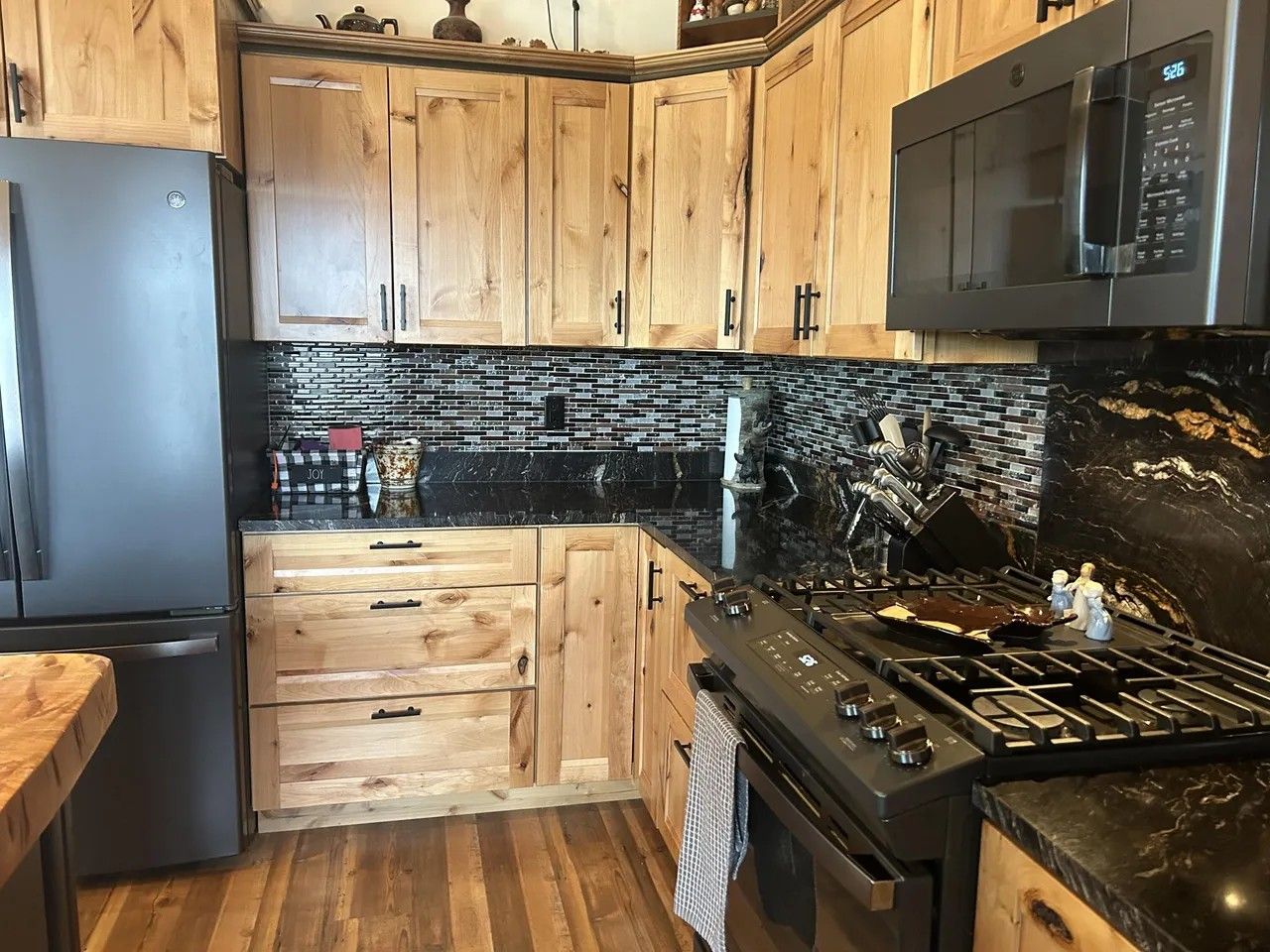 A kitchen with wooden cabinets, a black tiled backsplash, a stainless steel refrigerator, a microwave, and a gas stove.