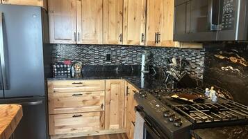 A kitchen with wooden cabinets, a black tiled backsplash, a stainless steel refrigerator, a microwave, and a gas stove.