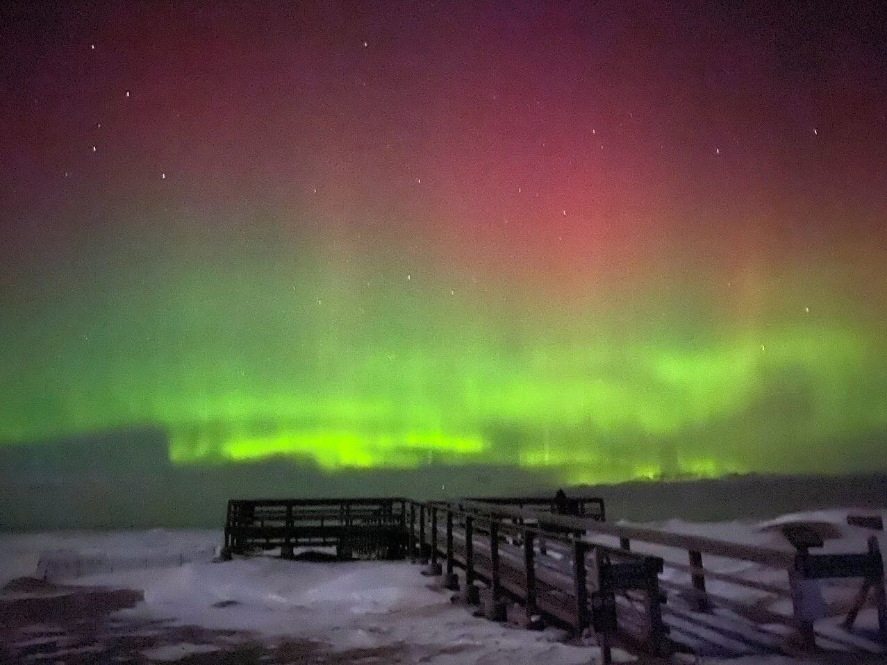 Ett snötäckt landskap med en träbrygga som sträcker sig ut i vattnet, under en stjärnklar natthimmel.