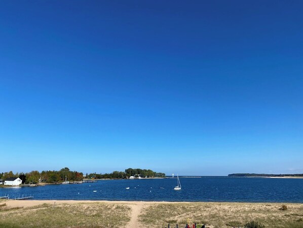 A coastal view with a sandy beach, a sailboat, and a distant shoreline with buildings and trees.