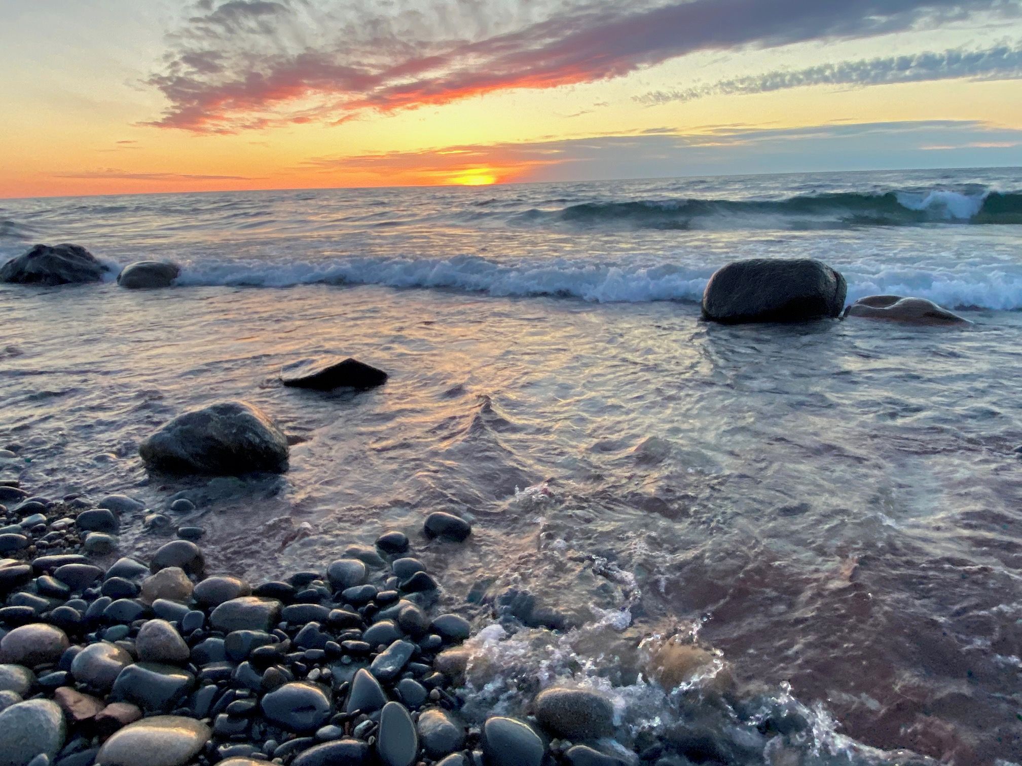 A beach with waves, pebbles, and a sunset.