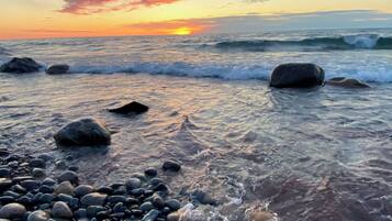 A beach with waves, pebbles, and a sunset.