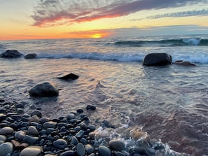 A beach with waves, pebbles, and a sunset.