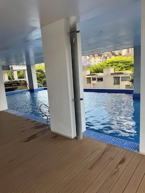 A swimming pool area with a wooden deck, a metal handrail, and a view of buildings and greenery in the background. - Gorgeous 1-bedroom apartment in Nairobi kilimani perfect for your stay (Nairobi)