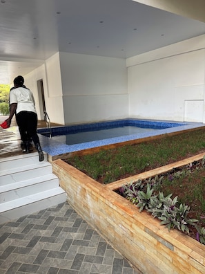 A person descending a staircase with a red object, leading to a pool area with a blue-tiled edge and a wooden border. - Gorgeous 1-bedroom apartment in Nairobi kilimani perfect for your stay (Nairobi)
