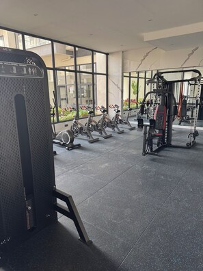 A gym with stationary bikes, a weight machine, and a large window. - Gorgeous 1-bedroom apartment in Nairobi kilimani perfect for your stay (Nairobi)