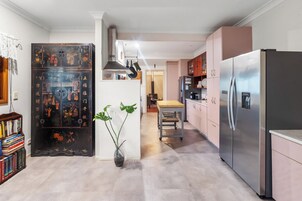 Una cocina moderna con un refrigerador de acero inoxidable, un comedor con mesa y sillas, y un mueble decorativo con obras de arte.