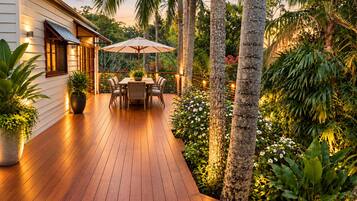 A wooden deck with a table and chairs, surrounded by tropical plants and palm trees.