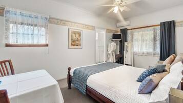 A hotel room with a bed, a table, a chair, a ceiling fan, and a shower area.