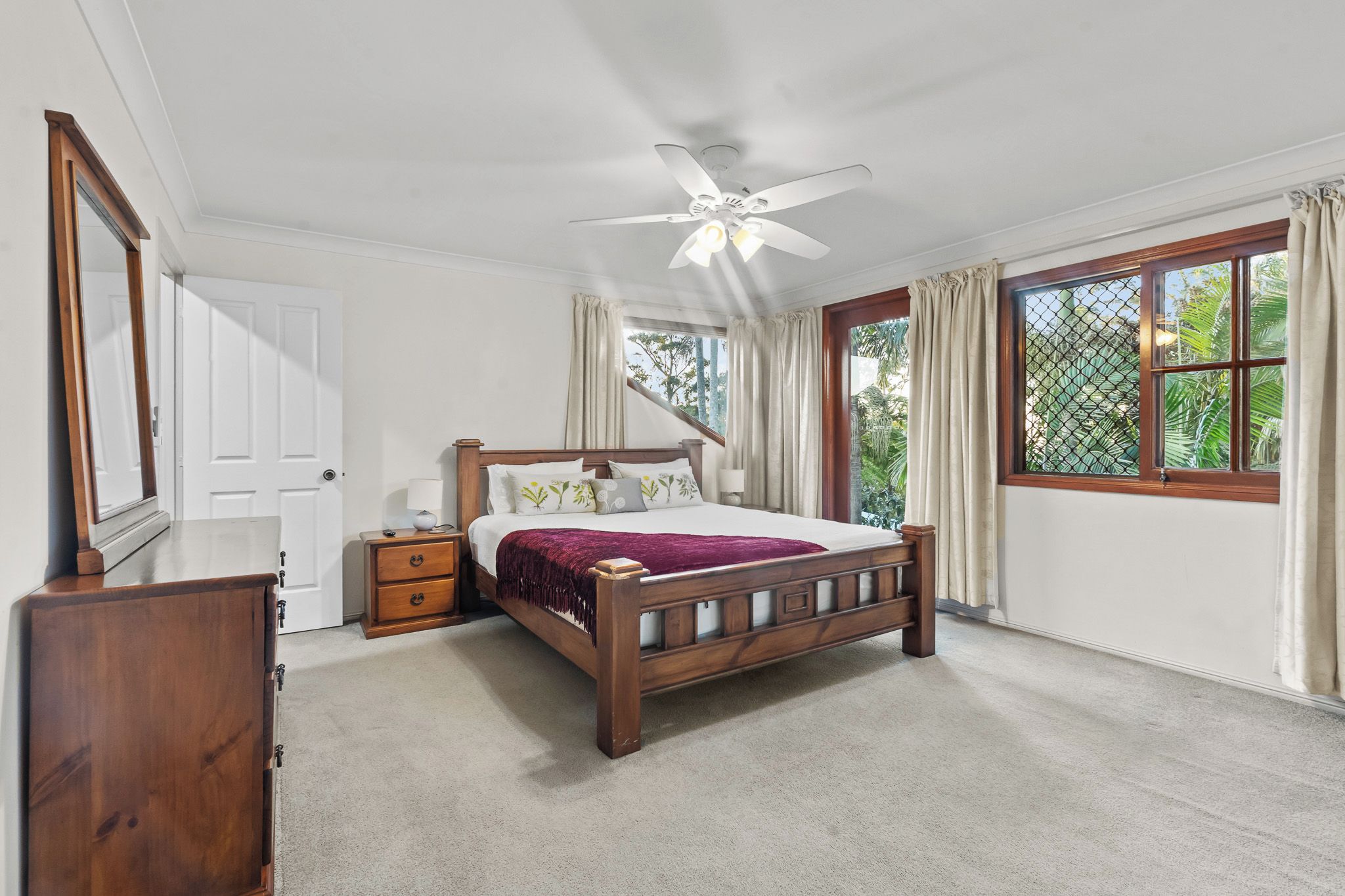 A bedroom with a wooden bed, a nightstand, a dresser, a ceiling fan, and a window with curtains.