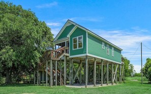 A green house with a wooden deck and a staircase leading to a porch.