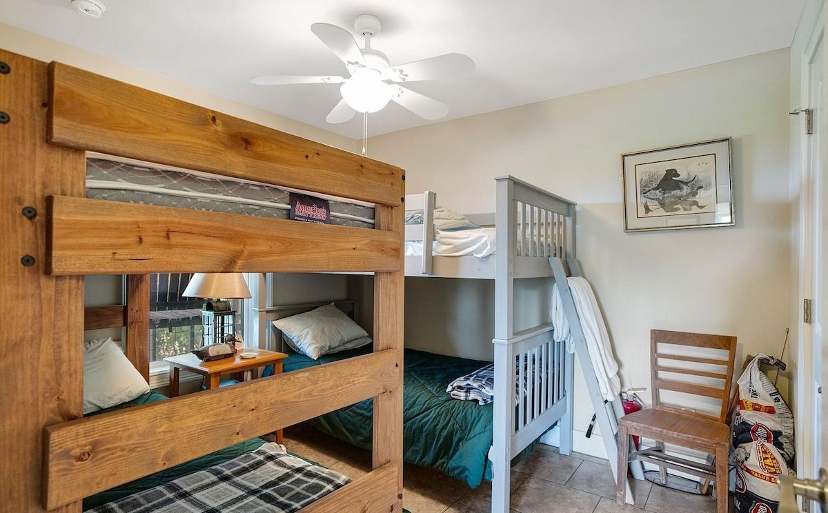 A bunk bed room with a ceiling fan, a framed picture on the wall, and a chair.