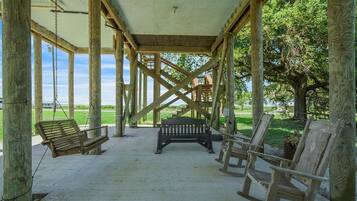 Un pavillon en bois installé à l’extérieur, équipé d’une balançoire, d’un banc et de chaises.