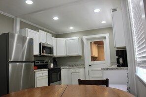 A kitchen with white cabinets, stainless steel appliances, a wooden table, and a window with blinds. - The Dettor House  (Sardis)