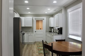 A kitchen with white cabinets, a refrigerator, a stove, a sink, and a window with blinds. - The Dettor House  (Sardis)