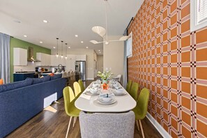 A modern kitchen with white cabinets, a stainless steel refrigerator, and a dining area with a white table set for four. - Retro Retreat | Hot Tub • Firepit • Near Lucas Oil (Indianapolis)