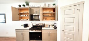 Una cocina con estufa, horno, microondas y armarios abiertos que contienen platos y vasos.