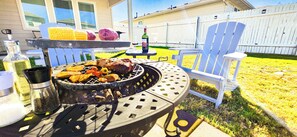 An outdoor grill with food, a bottle, and a chair. - Family & Group Vacations | 4 Bedrooms • Sleeps 10 • TXST • River • Outlets • Fire pit (San Marcos)