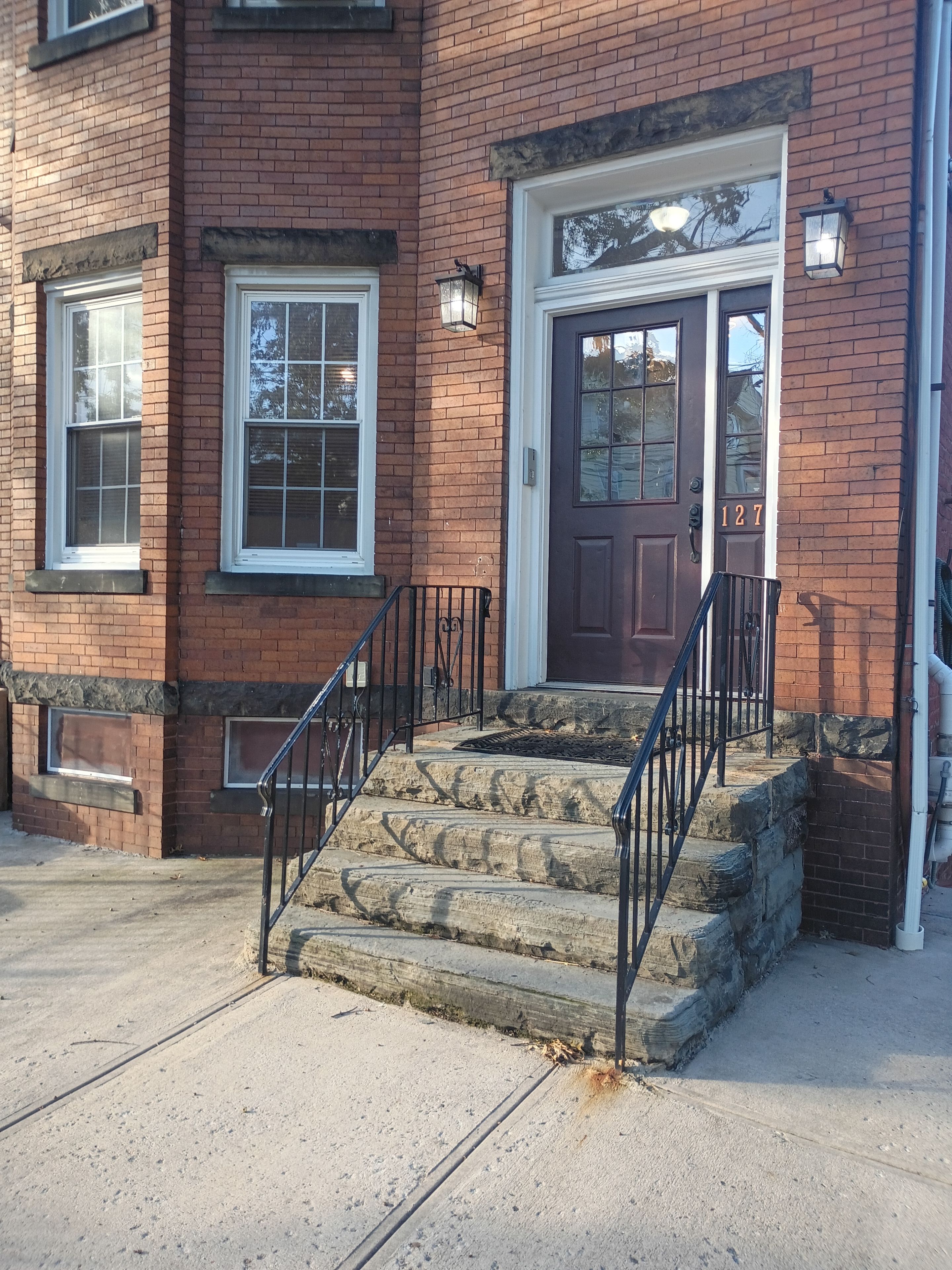 A brick building with a brown door, numbered 127, and a set of stone steps leading to the entrance.