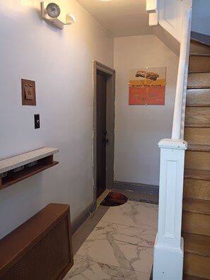 Ein Flur mit einer Tür, einem Schwarzebrett, einer Lampe und einer Holztreppe.