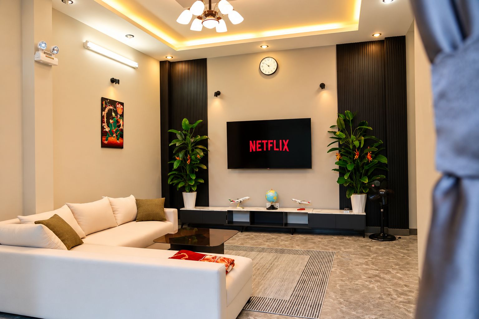 Ein modernes Wohnzimmer mit einem weißen Sofa, einem Flachbildfernseher, einer Uhr und zwei Blumentöpfen.