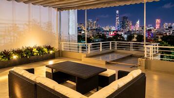 Eine Dachterrasse mit Gartenmöbeln, Blick auf eine nächtliche Skyline und einer Brüstung.