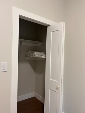 A closet with a white door, a wooden floor, and a shelf with folded clothes.