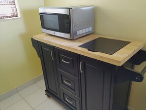 A kitchen area with a microwave on a wooden countertop, a black cabinet with drawers, and a tiled floor. - Lovely 2-bedroom condo on the beach, fully furnished. (Satellite Beach)