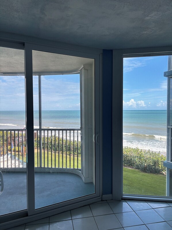 A balcony with a view of the ocean, a tiled floor, and a door leading to another room. - Lovely 2-bedroom condo on the beach, fully furnished. (Satellite Beach)
