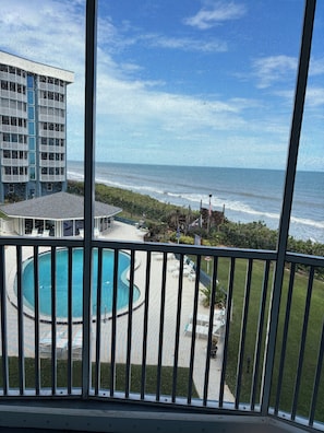 A pool area with a view of the ocean and a building in the background. - Lovely 2-bedroom condo on the beach, fully furnished. (Satellite Beach)