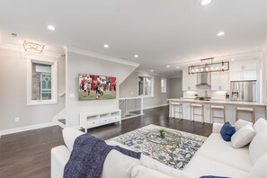 Una sala moderna con un sofá blanco, una mesa de centro y un televisor mostrando un partido deportivo.