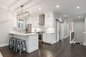A modern kitchen with white cabinetry, a central island with bar stools, and a stainless steel range hood. - Luxury 6BR Townhome Duplex - Family Stay (Columbus)
