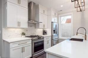 Cozinha moderna com armários brancos, eletrodomésticos de aço inoxidável e backsplash de mármore.