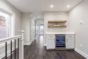 A modern kitchen with white cabinetry, a built-in wine cooler, and wooden shelves above the counter. - Luxury 6BR Townhome Duplex - Family Stay (Columbus)