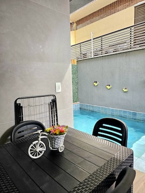 Ein Poolbereich mit Tisch und Stühlen, ein kleines weißes Fahrrad und ein Blumenkorb.