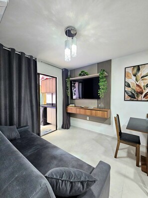 Ein modernes Wohnzimmer mit einem grauen Sofa, einem Esstisch mit Stühlen, einem flachbildfernseher an einer Holzkonsole und einem großen abstrakten Gemälde an der Wand.