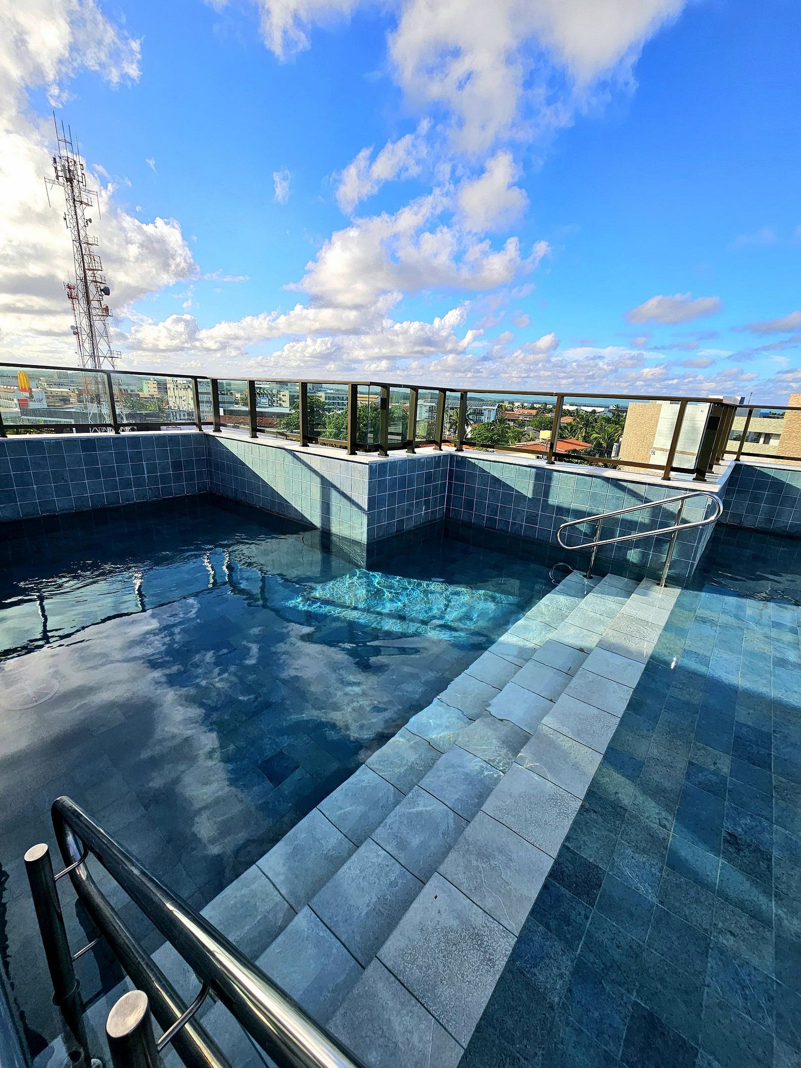 A rooftop pool with clear blue water, surrounded by glass railings and a tiled floor.