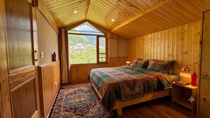Un dormitorio con paneles de madera, una cama grande, una ventana con vistas a follaje y una alfombra estampada.
