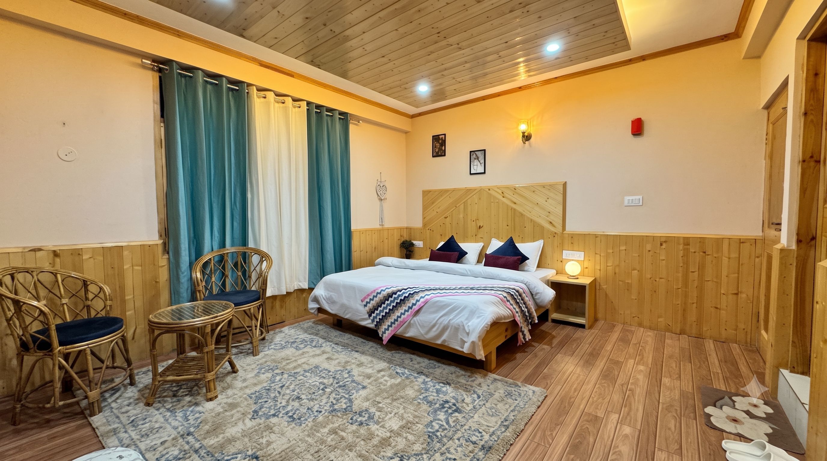 Un dormitorio con cabecera de madera, una cama con varias almohadas, una mesita de noche con lámpara, una silla y una ventana con cortinas.