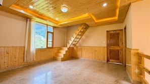 Una habitación con escalera de madera, un ventanal con vista a vegetación y una puerta con el número 06.