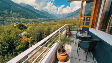 Un balcon donnant sur un paysage montagneux, une plante en pot et une table avec des chaises.